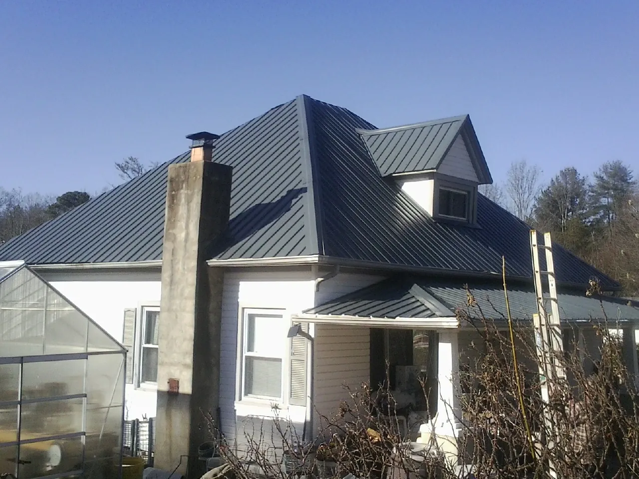 Dark blue standing seam metal roof on a white farmhouse with dormer — Slate & Tile Roof Repair by Roofing Brothers in Piney Woods