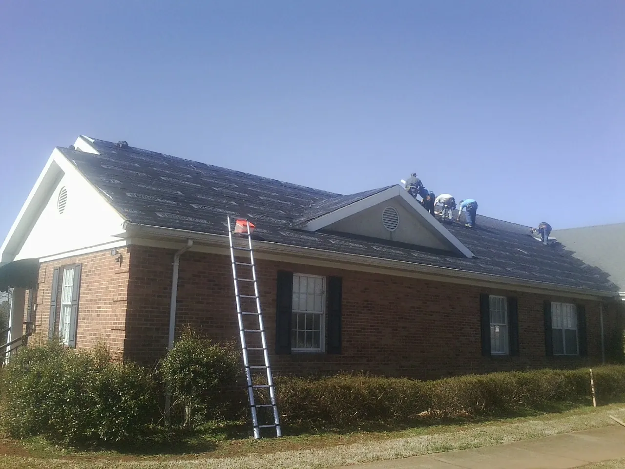 Crew tearing shingles off a brick ranch roof with a ladder set — Emergency Roof Repair work by our crew in Piney Woods