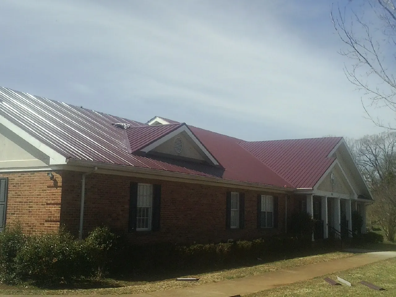 Red metal roof with gabled entries on a long brick building, from a Hail Damage Roof Repair job in Piney Woods