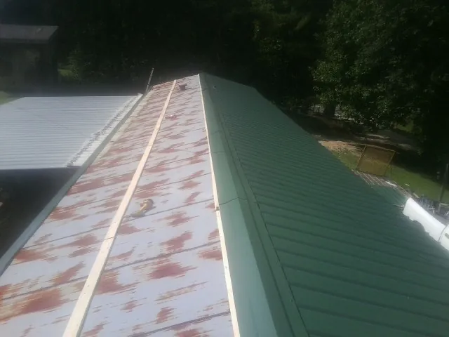 Old rusted panels beside newly installed green metal roofing — Wind Damage Roof Repair by Roofing Brothers in Piney Woods