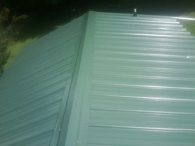 New green metal panels meeting at the ridge of a roof — Flat Roof Repair work by our crew in Piney Woods