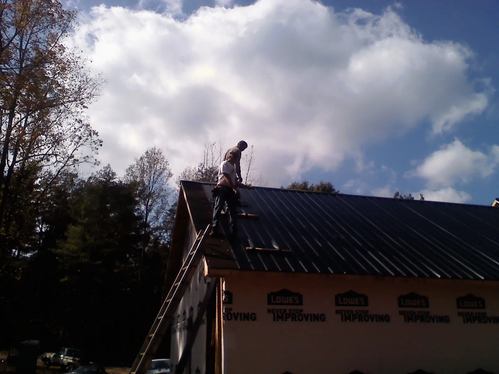 Roofer fastening dark metal panels high against a cloudy sky, from a Roof Inspection job in Piney Woods