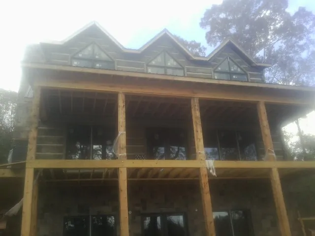 Dormers and porch framing on a large log home under construction — Roof Coating work by our crew in Piney Woods