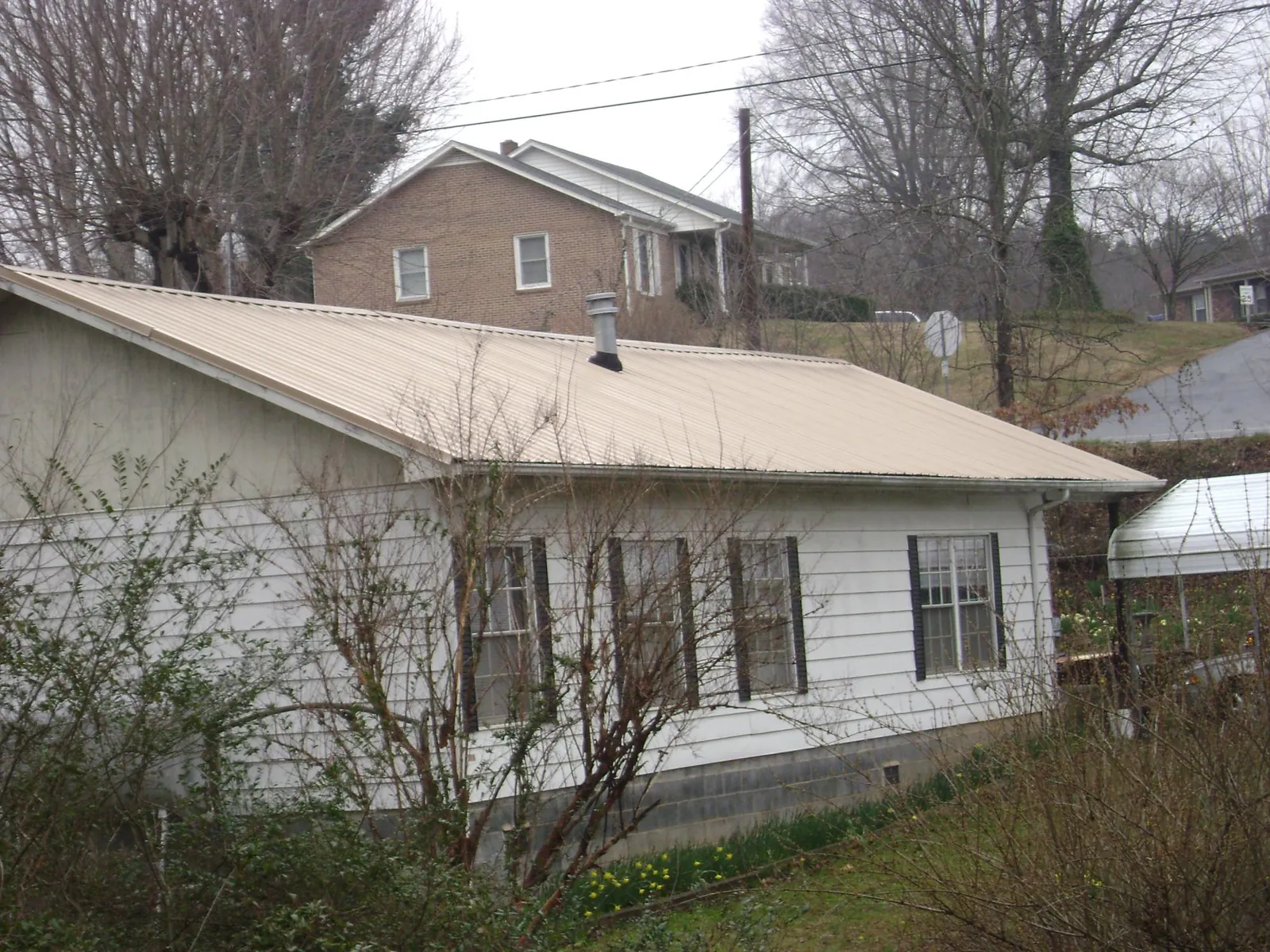Tan metal roof on a white sided house set into a hillside — Commercial Roofing by Roofing Brothers in Piney Woods
