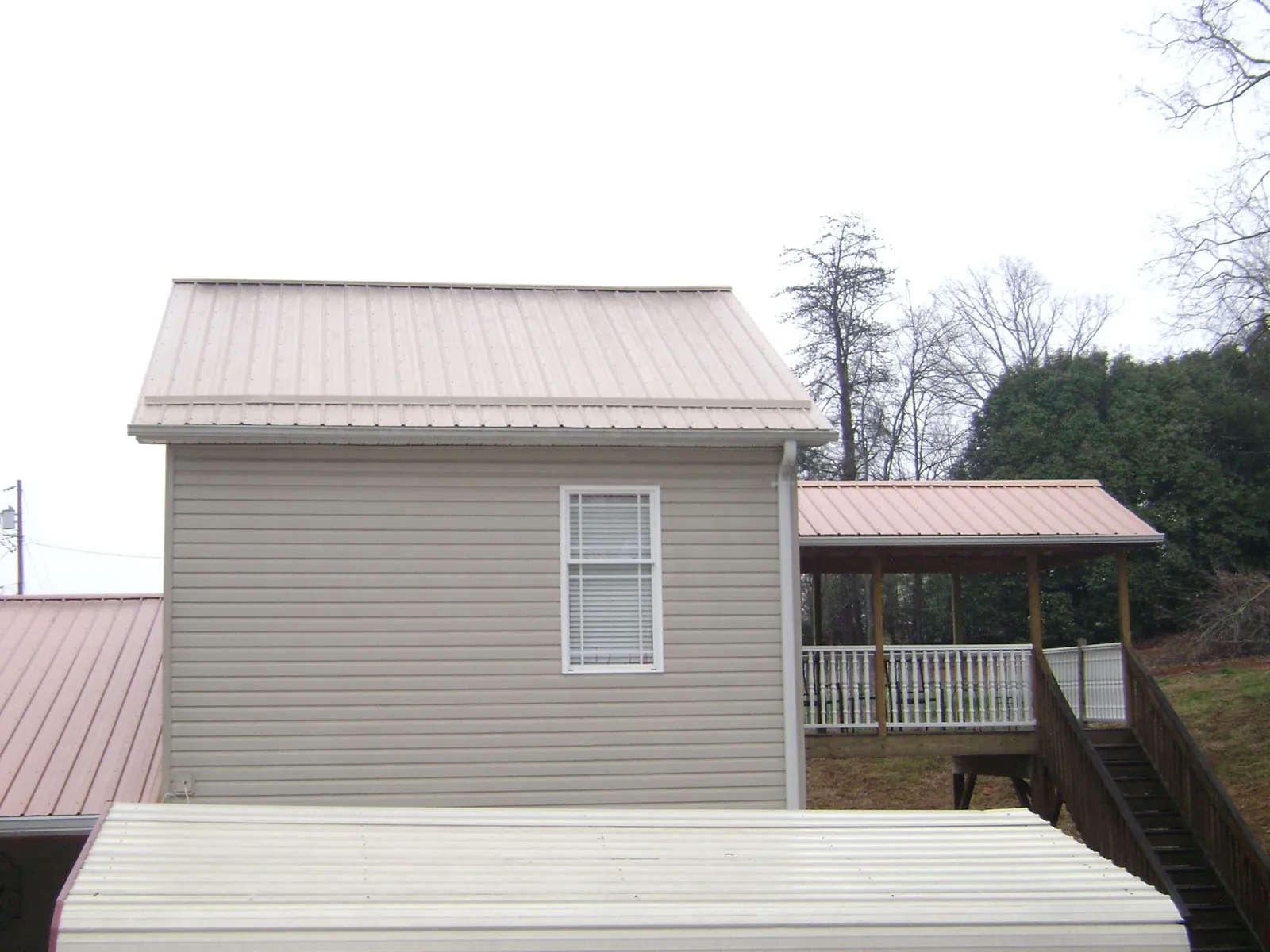 Tan metal roofs on a two story addition and attached porch, from a Roof Replacement job in Piney Woods